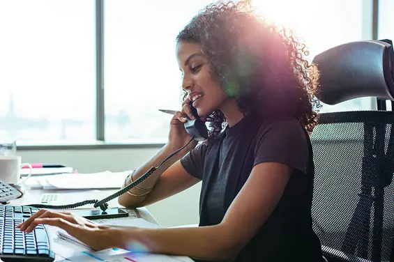 A woman on an office chair calling on desk phone